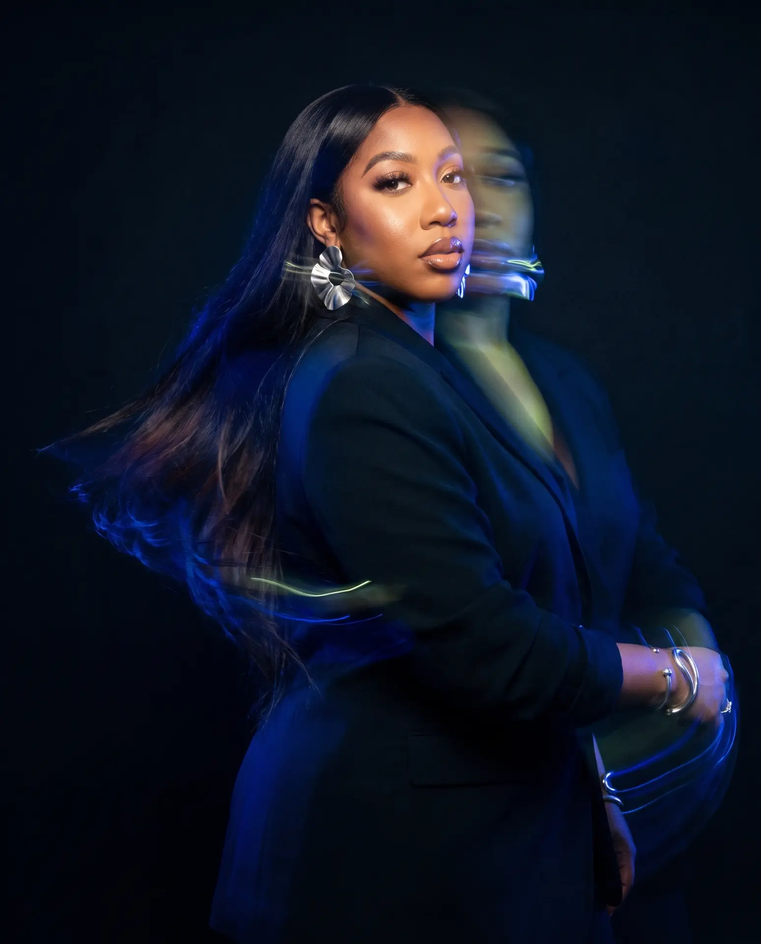 Kendah Lenée in a black suit, captured mid-turn with cobalt and lime motion-blur light trails